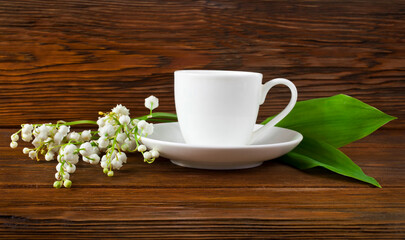 Cup of herbal tea with lily of the valley or may bells flowers on a wooden background. Copy space. 