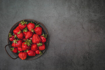 Delicious, fresh strawberries in a forged plate on a concrete background. Top view with space to copy.