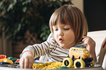Cute little boy playing with kinetic sand, toy car and tractor. Development of fine motor skills....