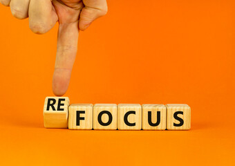 Focus or refocus symbol. Businessman turns wooden cubes and changes the concept word focus to refocus. Beautiful orange table orange background. Business focus or refocus concept. Copy space.