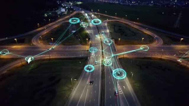 Self-driving autonomous cars move along a suburban traffic intersection in the evening. Neon HUD elements visualize the interaction of driverless cars connected to a common network and controlled remo