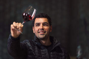 Man tasting red wine in a winery barrel cellar, holding a glass