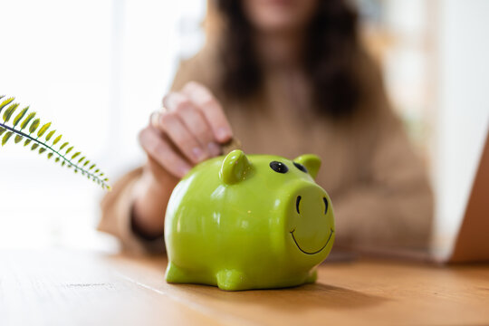 Close up young female putting coin in piggy bank. Woman saving money for household payments, utility bills, calculating monthly family budgets, making investments or strategy for personal savings