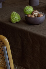 Elegant table setting with cherimoya fruits, brown champignons in craft ceramic plate on linen tablecloth. Outdoor table setting for summer holiday concept.