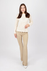 Beauty, fashion and makeup concept. Beautiful long hair brunette woman portrait with white sweater, classic white shoes and beige tight trousers. Studio shot. Model looking to camera with smile
