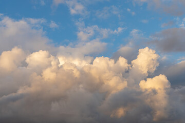 Cumulonimbus clouds against the blue sky. Picturesque cumulus clouds in the yellow light of the...