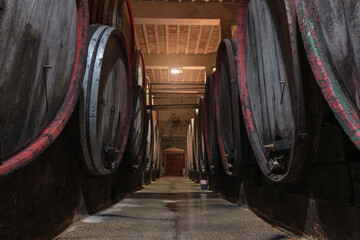 The ambiance of the traditional wine cellar, aging red wine barrels, wooden casks in rows in the winery underground storage room