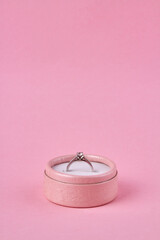 Vertical shot of pink gift box with engagement ring on pink background. Space for text.