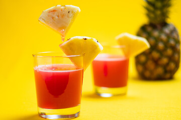 Pineapple juice in glass closeup near sliced fruit with spash and dripping liqid for summer vibes.