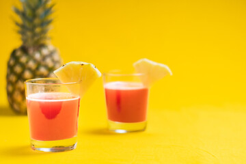 Pineapple juice in glass closeup near sliced fruit with spash and dripping liqid for summer vibes.