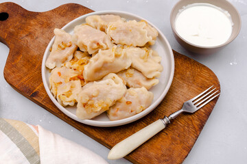 Homemade dumplings, vareniki, varenyky, pyrohy with stewed cabbage fried with onion on plate.Traditional ukrainian popular national dish,cuisine served with sour cream on wooden board, gray backgound