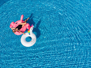 Beautiful summer background. Woman on flamingo pool float and unicorn in pool. Summer holidays, enjoying summer vacations during quarantine.
