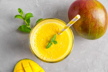 Fresh yellow mango smoothie in a glass with straw, fresh fruits and mint. Summer tropical drink