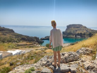 Young blonde woman looking on bay and sea beach on Greece island Rhodes. Lindos city