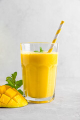 Fresh yellow mango smoothie in a glass with straw, fresh fruits and mint. Summer tropical drink