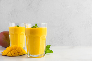 Mango smoothie in glasses with fresh fruits. Summer tropical drink on white background