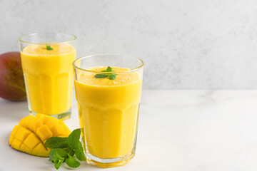 Fresh yellow mango smoothie in glasses with fresh fruits and mint. Summer tropical drink on white background