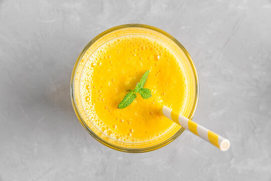 Fresh yellow summer mango smoothie in a glass with a straw and mint on gray concrete table. Top view