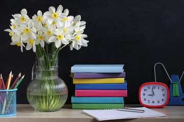 daffodils, textbooks and an alarm clock on the background of a blackboard.