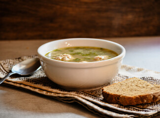 Homemade appetizing, delicious soup with meatballs, homemade bread, kitchen national napkin, and spoon on the kitchen dining table.