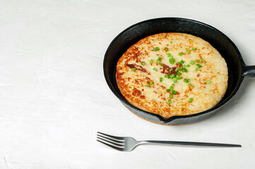 A Swiss traditional dish is a potato pancake in a frying pan, decorated with green onions, with a fork next to it. copy space.