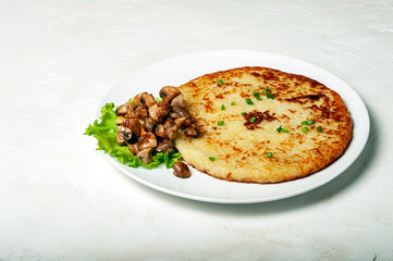 traditional Swiss dish is a potato pancake on a white plate with fried mushrooms and a leaf of green salad, side view.