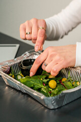 In a disposable dish is a green salad with various leaves and olives. Girl pours honey salad, eating in the office, the concept of healthy eating. The concept of ecological utensils