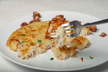 on the fork is a piece of potato tortilla - a traditional Swiss dish, the fork is raised above a plate with a half-eaten potato tortilla and fried mushrooms. leftovers on plates after meals.