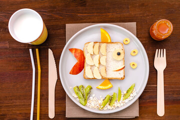 Funny cute fish shape sandwich toast bread with banana, apple,orange, milk,honey. Kids childrens baby's sweet dessert healthy breakfast lunch food art on plate,wooden background close up,top view