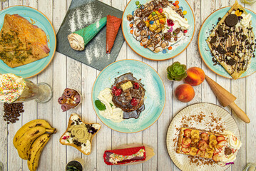 Top view image of desserts, ice creams and plates with sweets, fruits, creams, cream and chocolate, crepe with syrup and cookies