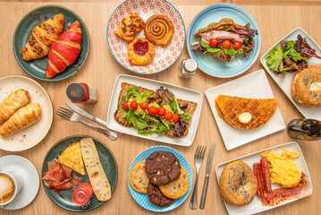 Fototapeta na wymiar Overhead view of a set of dessert plates, cinnamon roll, cookies, assorted croissants, lettuce sandwiches, chocolate chips, and egg breakfasts