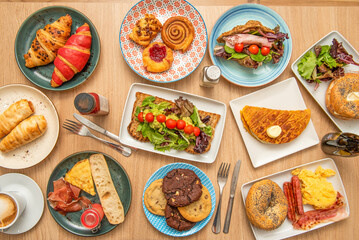 Overhead view of a set of dessert plates, cinnamon roll, cookies, assorted croissants, lettuce sandwiches, chocolate chips, and egg breakfasts