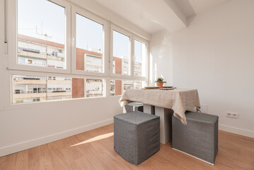 Living room with a dining table with a linen tablecloth next to a large window on a clear spring day