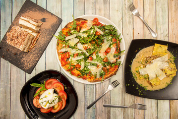 Set of Italian dishes with Neapolitan pizza with a lot of arugula, burrata salad with tomato and olive oil, ravioli with cheese and sauce and tiramisu for dessert