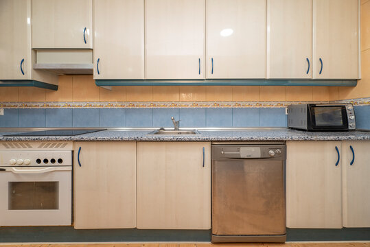 Front image of a kitchen with shiny wooden furniture, a countertop with blue accents that match the skirting board and borders