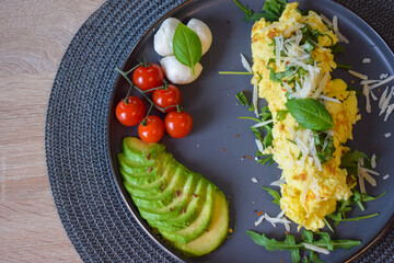 French omelette dish. Delicous homemade french omlette filled with cheese. Plating with fresh vegetables like avocado, cherry tomatoes, but also basil and mozzarella.