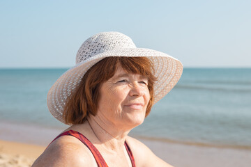 Satisfied face of an elderly woman in a hat on the seashore on a sunny day, close-up.Happy summer days