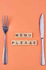 The inscription Menu please on wooden cubes with cutlery on color background. Top view and flat lay.