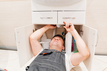 A male plumber repairs siphon under the sink in the bathroom.
