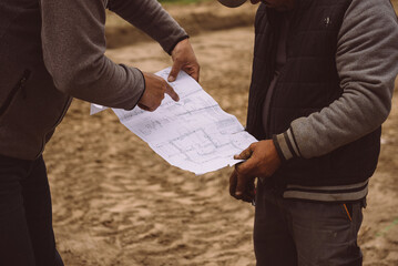 Architect showing house build plans at the building site. Engineer working with blueprints outside...