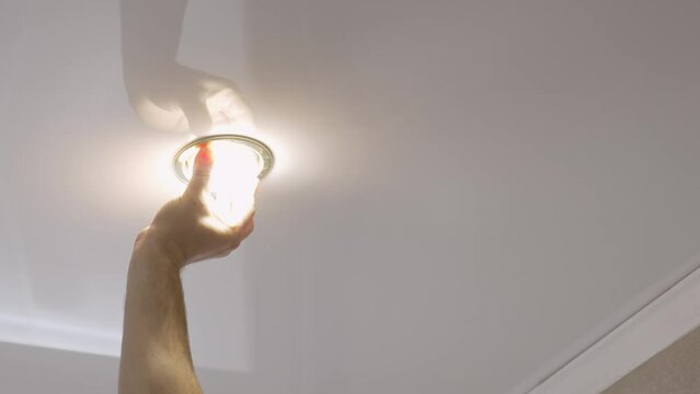 A male electrician changes the light bulbs in the spotlight ceiling lamp