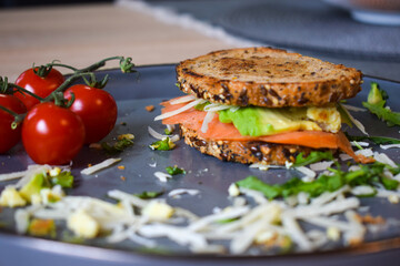 Homemade delicious roasted crisp sandwich with toast, salmon and avocado. Served on the side with Grana Padano or Parmigiano (Parmesan) cheese and Cherry Tomatoes.