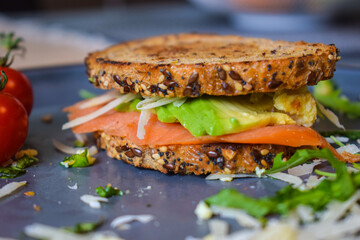 Homemade delicious roasted crisp sandwich with toast, salmon and avocado. Served on the side with Grana Padano or Parmigiano (Parmesan) cheese and Cherry Tomatoes.