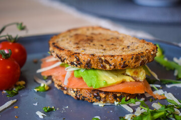 Homemade delicious roasted crisp sandwich with toast, salmon and avocado. Served on the side with Grana Padano or Parmigiano (Parmesan) cheese and Cherry Tomatoes.