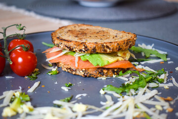 Homemade delicious roasted crisp sandwich with toast, salmon and avocado. Served on the side with Grana Padano or Parmigiano (Parmesan) cheese and Cherry Tomatoes.