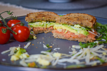 Homemade delicious roasted crisp sandwich with toast, salmon and avocado. Served on the side with Grana Padano or Parmigiano (Parmesan) cheese and Cherry Tomatoes.