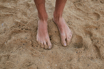 The guy stands on the sand barefoot. Legs close up. Sea. Ocean