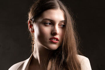 Portrait of a young brunette with long hair in the studio. Dramatic photo in dark colors.