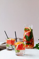 two glasses of Grapefruit juice with green mint on beige background. Cocktail fresh grapefruit with tequila. Two glasses of grapefruit lemonade. Refreshing summer drinks. vertical.copy space