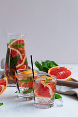 two glasses of Cocktail grapefruit with fruits. fresh Grapefruit juice with green mint on beige background. Glass and jug of grapefruit lemonade. Refreshing summer drinks. copy space. vertical.